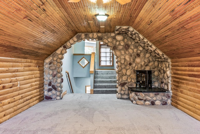 unfurnished living room featuring log walls, a wood stove, carpet, stairway, and a ceiling fan