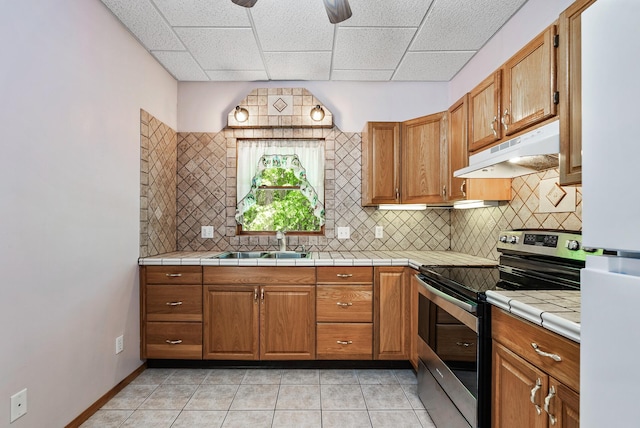 kitchen with stainless steel electric range, under cabinet range hood, a sink, tasteful backsplash, and freestanding refrigerator