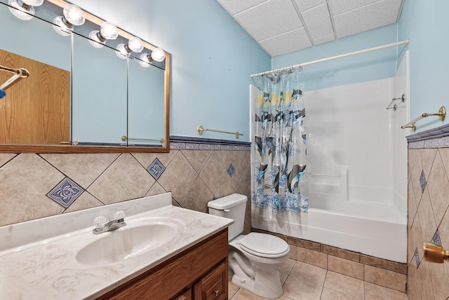 bathroom with toilet, a paneled ceiling, tile walls, shower / bath combination with curtain, and tile patterned flooring