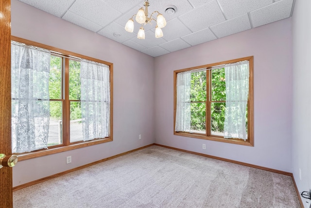 carpeted empty room featuring a chandelier, baseboards, and a drop ceiling