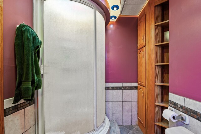 bathroom featuring a shower stall, tile patterned flooring, tile walls, built in shelves, and wainscoting