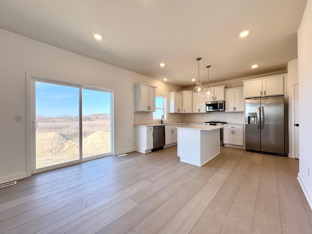 kitchen with appliances with stainless steel finishes, light countertops, backsplash, light wood finished floors, and a center island