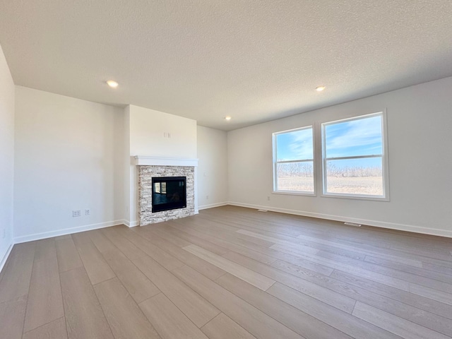 unfurnished living room featuring dark wood-style flooring, recessed lighting, a textured ceiling, a stone fireplace, and baseboards