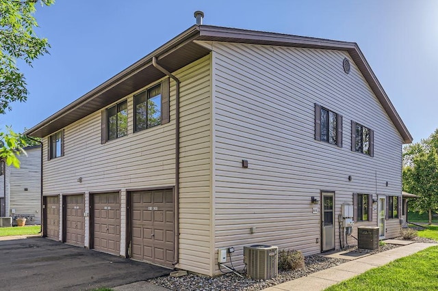 view of property exterior featuring central AC, asphalt driveway, and a garage