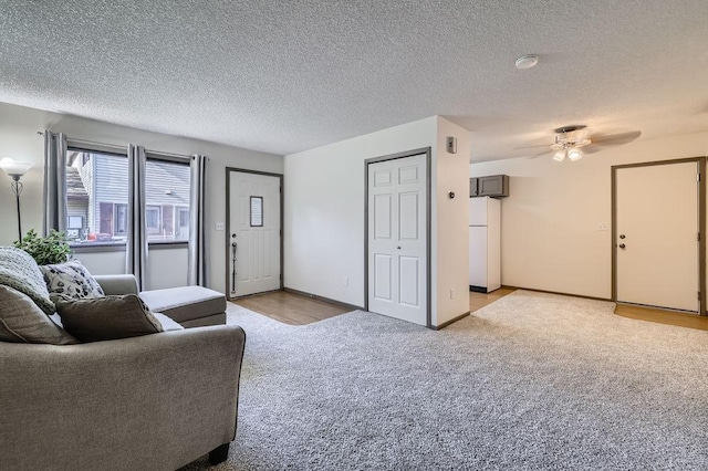 living area featuring light carpet, ceiling fan, a textured ceiling, and baseboards