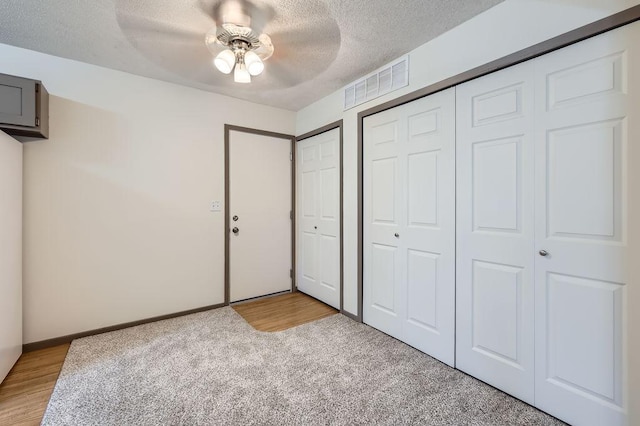 unfurnished bedroom with a textured ceiling, light carpet, two closets, a ceiling fan, and baseboards