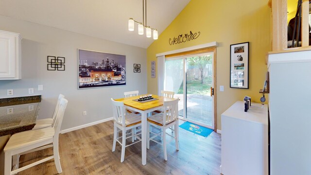 dining space with light wood-style floors, baseboards, and high vaulted ceiling