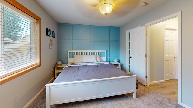 carpeted bedroom with a decorative wall, ceiling fan, and baseboards