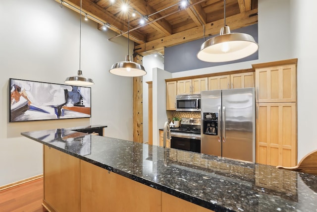 kitchen with appliances with stainless steel finishes, wooden ceiling with exposed beams, rail lighting, wood finished floors, and dark stone counters