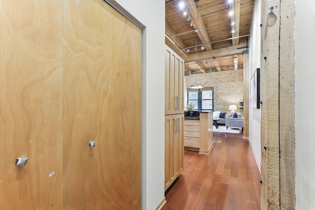 corridor with wooden ceiling with exposed beams, wood finished floors, and brick wall