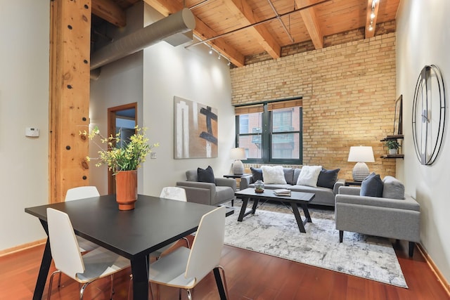 living area with wood ceiling with exposed beams, brick wall, rail lighting, wood finished floors, and baseboards
