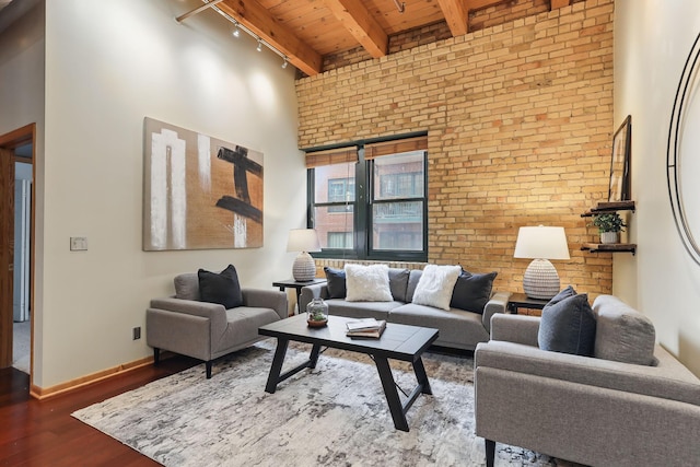 living area featuring rail lighting, wood ceiling with exposed beams, brick wall, wood finished floors, and a high ceiling
