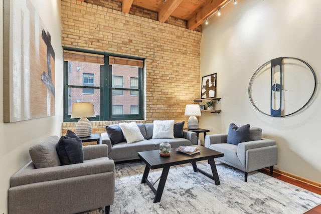 living area with brick wall, wooden ceiling with exposed beams, track lighting, a high ceiling, and wood finished floors