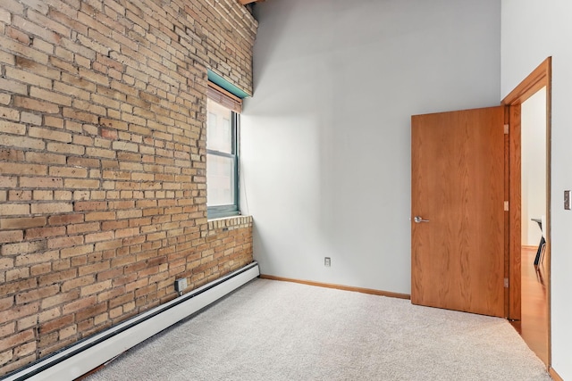 empty room featuring a baseboard heating unit, brick wall, carpet floors, baseboards, and a towering ceiling