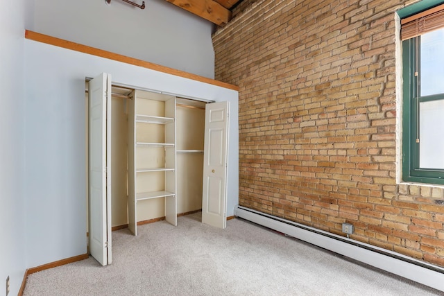 unfurnished bedroom featuring baseboard heating, light colored carpet, brick wall, baseboards, and a closet
