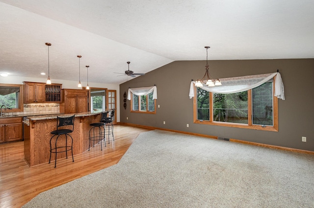 kitchen with brown cabinets, a sink, open floor plan, baseboards, and vaulted ceiling