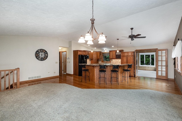 kitchen featuring brown cabinets, a breakfast bar area, carpet floors, lofted ceiling, and decorative backsplash
