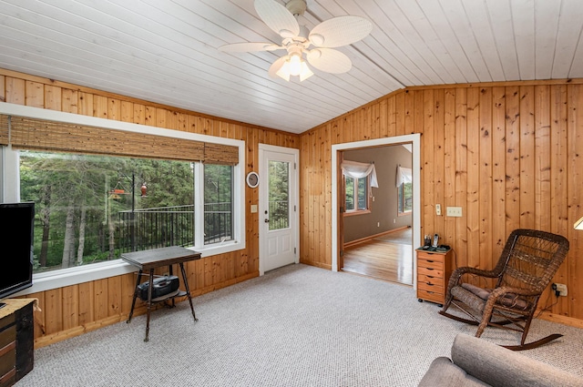 sitting room with plenty of natural light, lofted ceiling, wooden walls, light carpet, and a ceiling fan