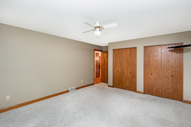 unfurnished bedroom featuring two closets, carpet, baseboards, and a ceiling fan