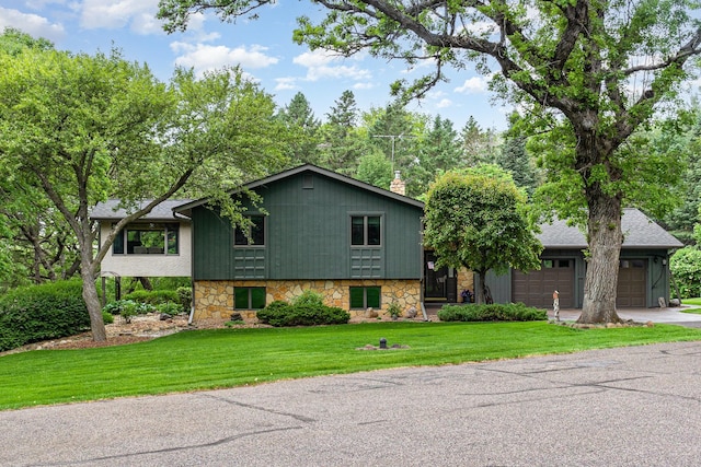 tri-level home with concrete driveway, stone siding, a front yard, a garage, and a chimney