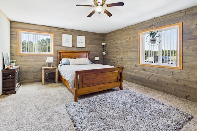 carpeted bedroom featuring wood walls and a ceiling fan