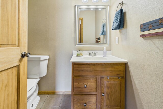 half bath featuring tile patterned floors, toilet, vanity, and baseboards