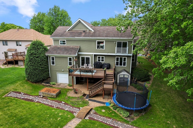rear view of house featuring a trampoline, a wooden deck, stairs, a lawn, and a shingled roof