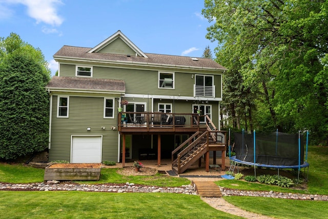 rear view of house with a wooden deck, stairway, a lawn, a trampoline, and roof with shingles
