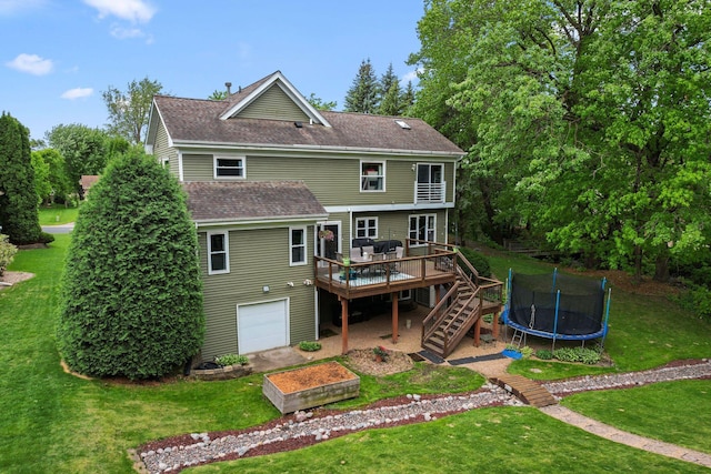 back of house featuring roof with shingles, a wooden deck, a lawn, a trampoline, and stairs