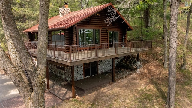 rear view of property featuring a chimney, log exterior, stone siding, a deck, and metal roof