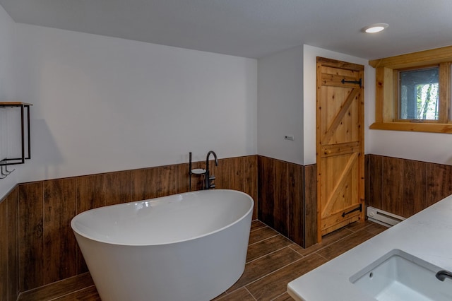 bathroom with a baseboard heating unit, wainscoting, a soaking tub, a sink, and wood tiled floors