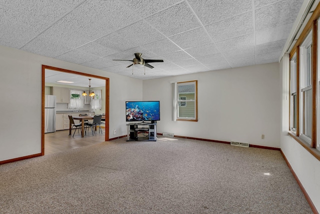 carpeted living area featuring ceiling fan, baseboards, a chandelier, and a drop ceiling