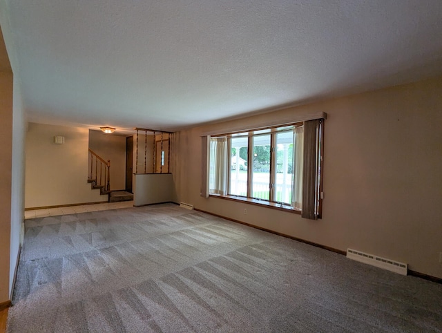 unfurnished living room with a baseboard heating unit, stairs, light colored carpet, baseboards, and a textured ceiling
