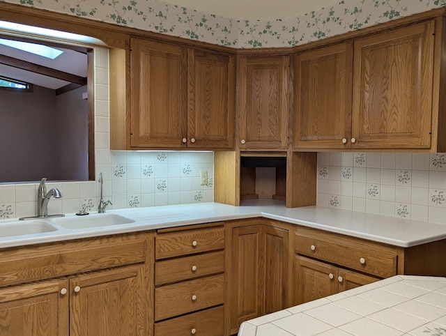 kitchen with brown cabinetry, light countertops, tasteful backsplash, and a sink