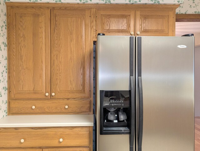 kitchen featuring stainless steel refrigerator with ice dispenser, wallpapered walls, light countertops, and brown cabinets