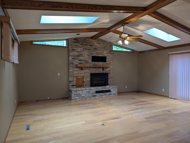 unfurnished living room featuring a skylight, light wood-style floors, a brick fireplace, and a ceiling fan