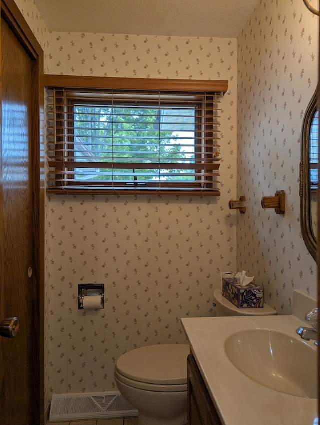 half bath featuring wallpapered walls, toilet, and vanity