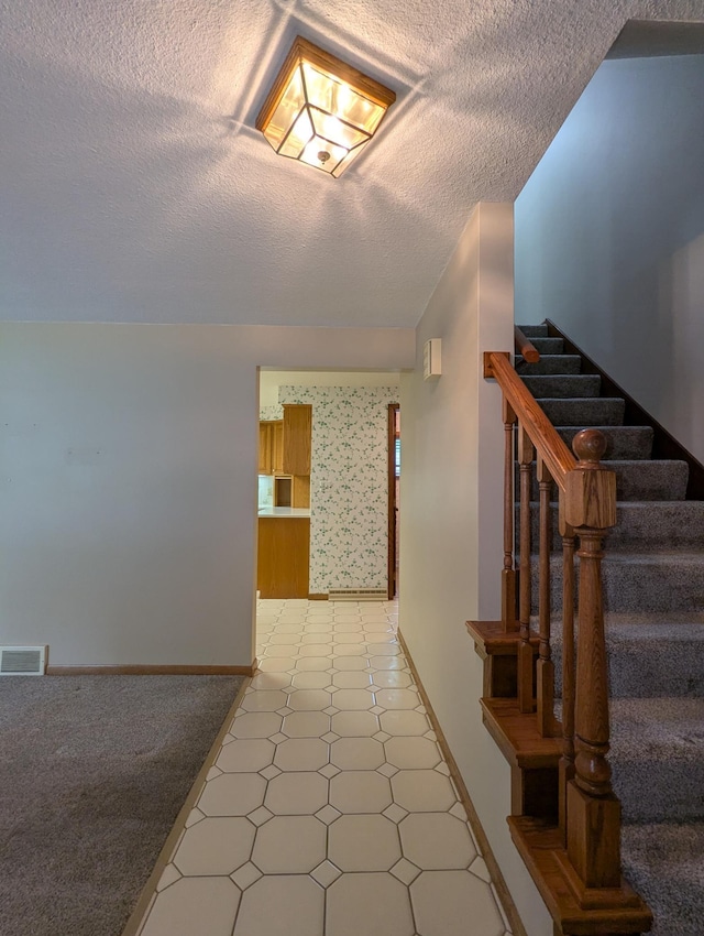 hallway featuring light floors, a textured ceiling, stairs, and baseboards