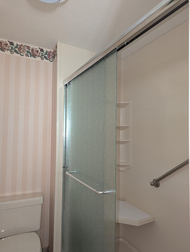 bathroom with wallpapered walls, a stall shower, and toilet