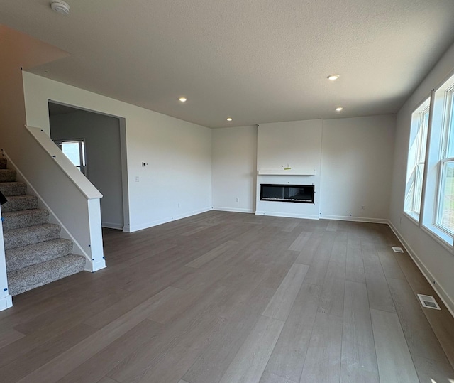 14605 74th St NE, Otsego, MN 55330 - unfurnished living room with wood finished floors, stairway, a glass covered fireplace, recessed lighting, and a textured ceiling