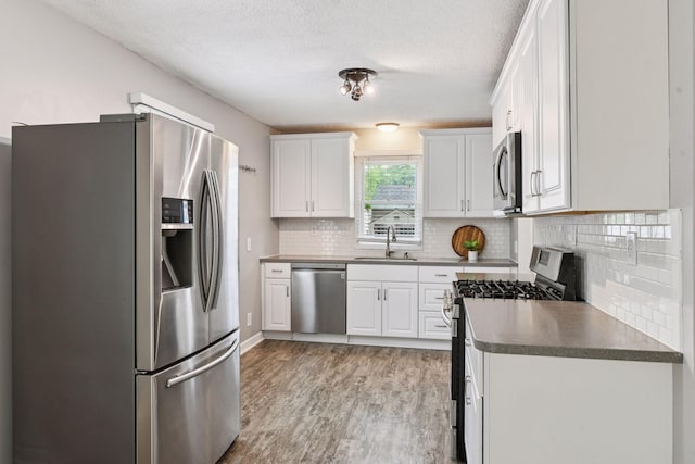 426 14th Ave N, Hopkins, MN 55343 - kitchen featuring stainless steel appliances, dark countertops, a sink, light wood-style floors, and backsplash