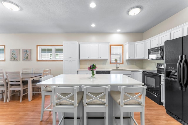 2737 Faulkner Dr, Chaska, MN 55318 - kitchen with black appliances, a breakfast bar area, white cabinets, light wood-type flooring, and light countertops