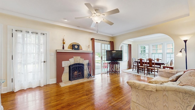 living room with arched walkways, wood finished floors, a fireplace with flush hearth, and a ceiling fan