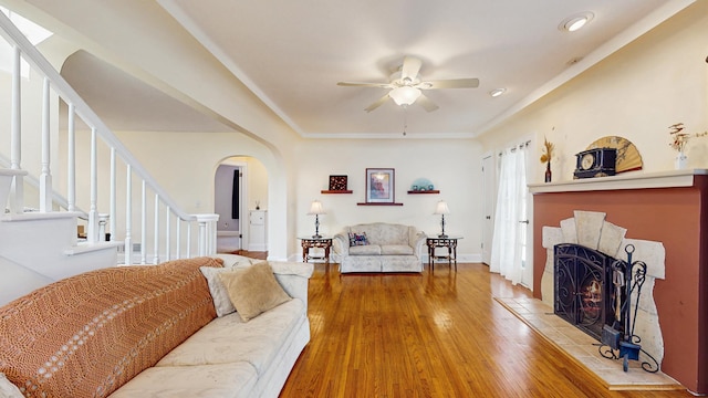 living area with arched walkways, ceiling fan, hardwood / wood-style floors, stairway, and baseboards