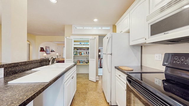 kitchen with black electric range, white microwave, a sink, dark countertops, and white cabinetry