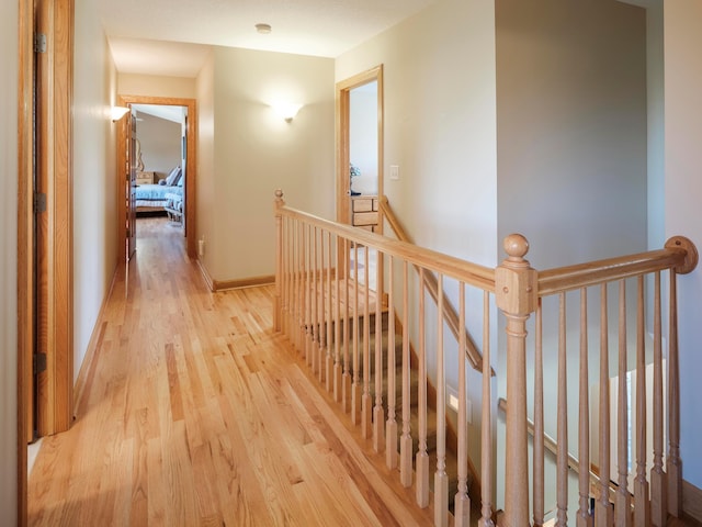 hallway featuring an upstairs landing, light wood finished floors, and baseboards