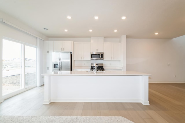 kitchen featuring appliances with stainless steel finishes, light wood-style flooring, a kitchen island with sink, white cabinets, and recessed lighting
