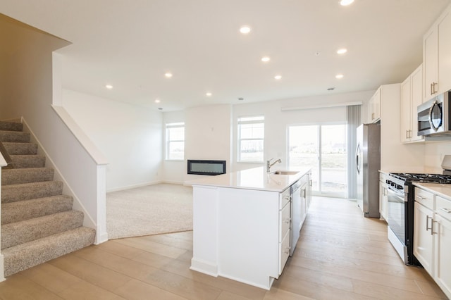 kitchen featuring appliances with stainless steel finishes, a sink, light wood finished floors, recessed lighting, and open floor plan