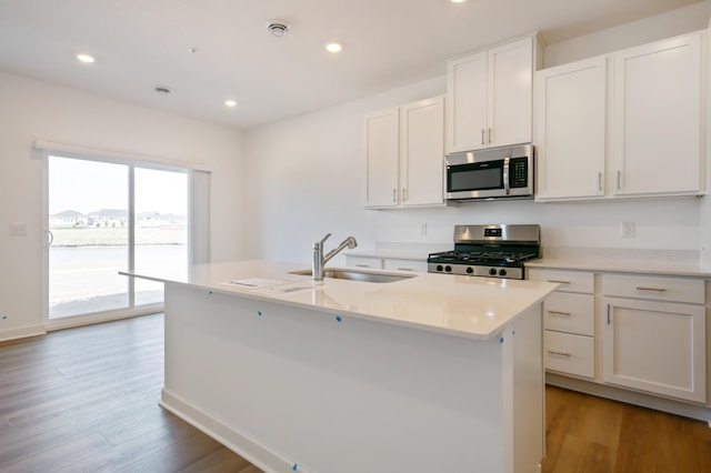 kitchen featuring stainless steel appliances, a sink, light wood-style flooring, light countertops, and a kitchen island with sink