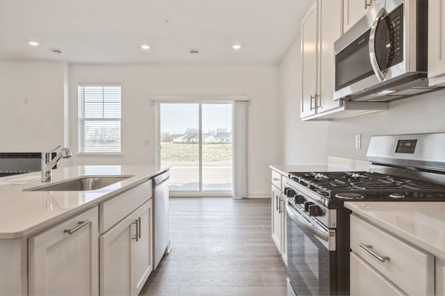 kitchen featuring stainless steel appliances, a sink, light countertops, recessed lighting, and white cabinetry
